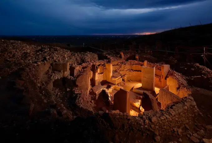 The excavated stone enclosure at Gobeklitepe lit at dusk.