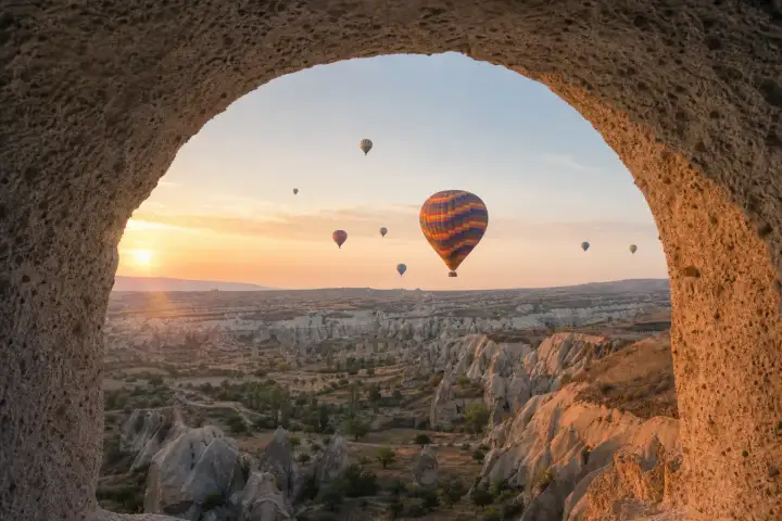 Hot air balloons above Cappadocia valleys framed by a traditional weathered stone arch.