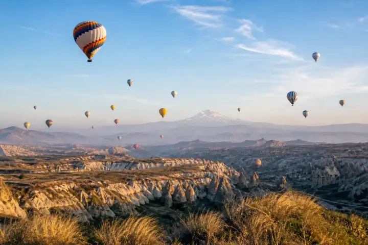 Hot air balloons above Cappadocia valleys with snow-covered Mount Erciyes on the horizon.