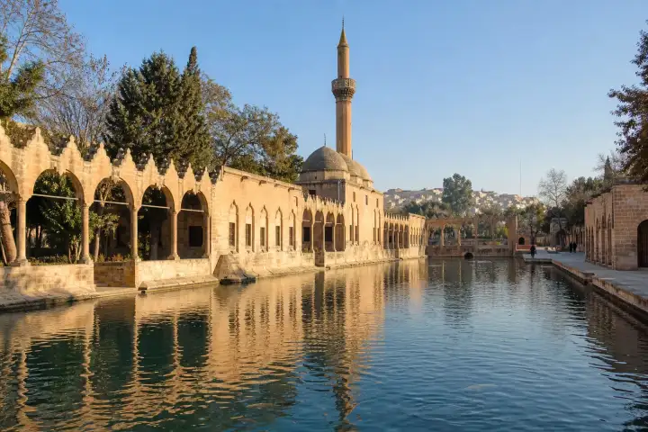 Balıklıgöl and the stone arcades of Rizvaniye Mosque in Şanlıurfa at sunrise.