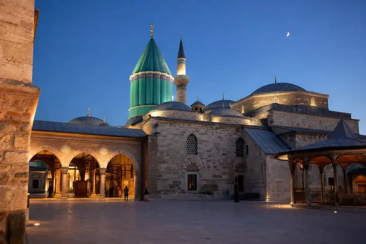 The turquoise dome and stone courtyard of the Mevlana Museum in Konya at blue hour.