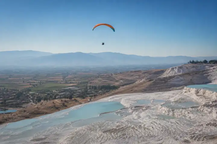 A tandem paraglider soaring above the white travertine terraces of Pamukkale.