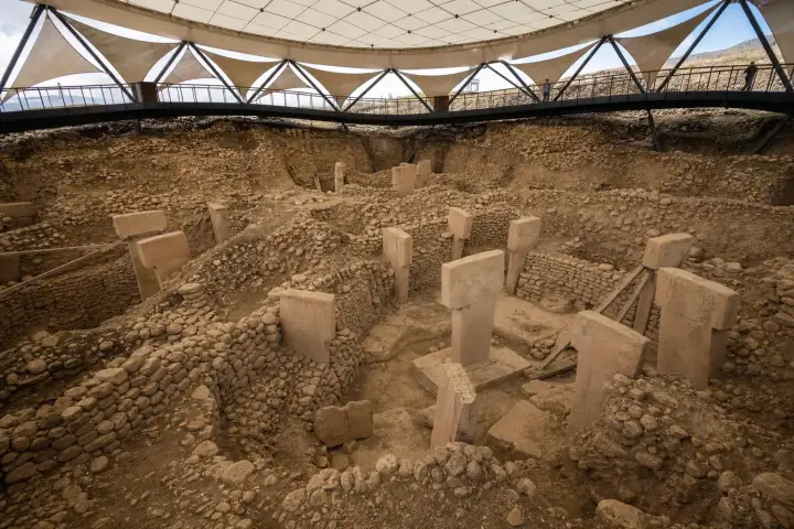 Weathered T-shaped pillars within a Göbeklitepe enclosure beneath the protective shelter.