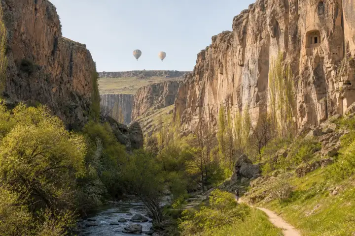 The Melendiz stream and spring trail through Ihlara Valley beneath distant hot air balloons.
