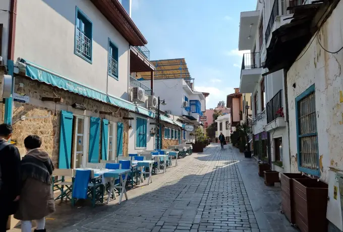 A cobbled lane in Antalya's Kaleici quarter runs between whitewashed houses with turquoise shutters, cafe tables set out on the pavement in the winter sun.