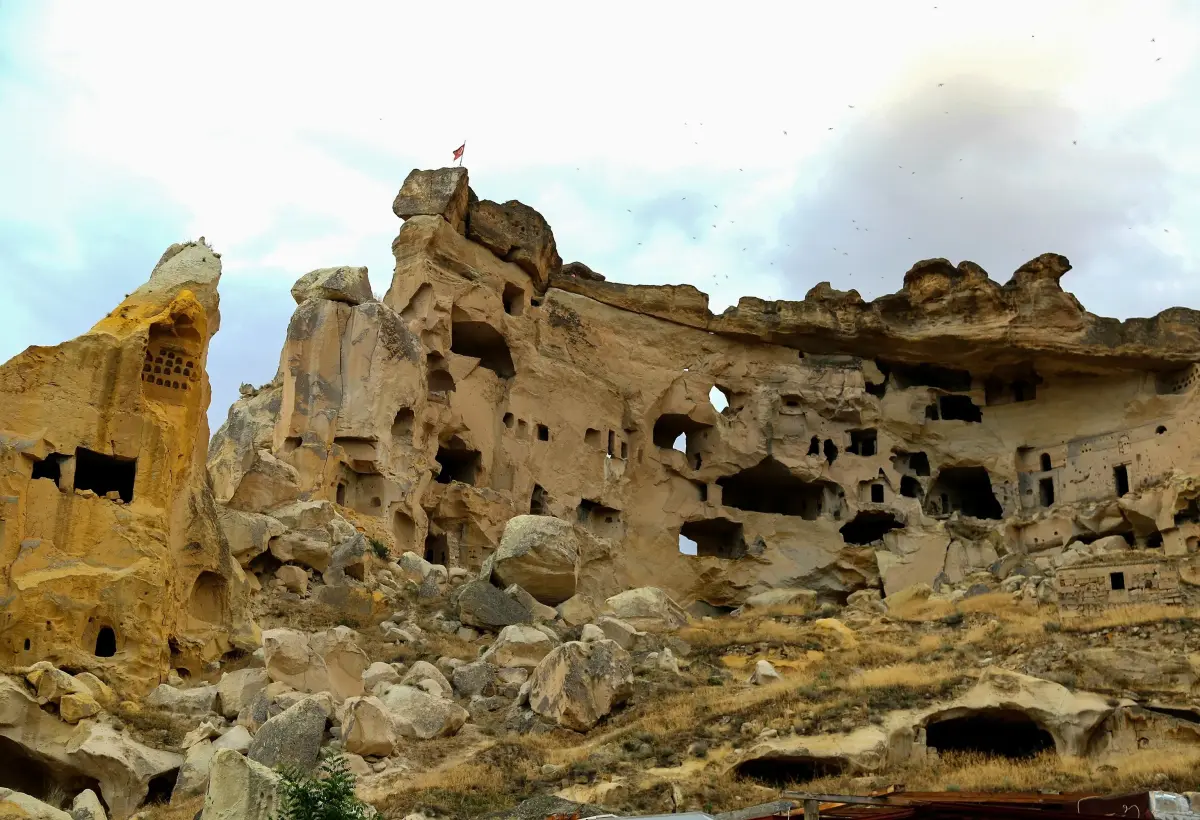A tall rock outcrop in Cappadocia is honeycombed with cave rooms and windows on several levels, fallen blocks scattered along its base.