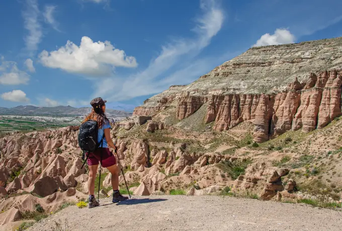 A hiker with a backpack pauses on a pale ridge above the folded pink cliffs of Rose Valley in Cappadocia.
