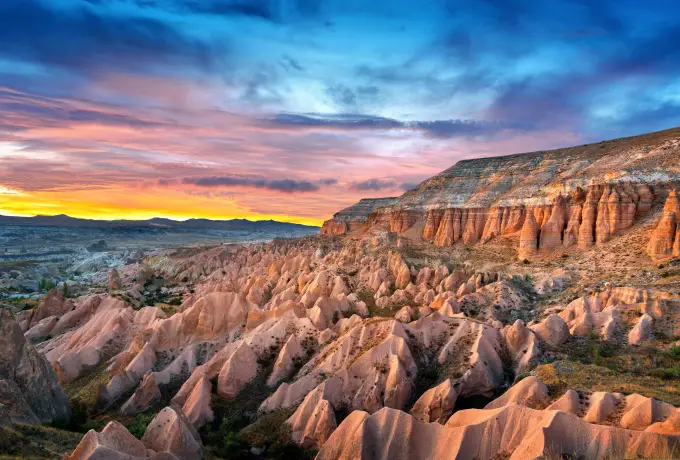 Sunset light rakes the folded pink and orange ridges of Rose Valley in Cappadocia under a band of coloured cloud.