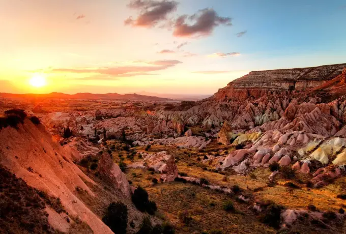 The sun sets over Red Valley in Cappadocia, lighting the folded red and orange ridges from the side.
