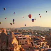 Dozens of hot air balloons spread across the morning sky above the cave-cut houses and rock cones of a Cappadocia town.