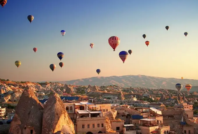 Dozens of hot air balloons spread across the morning sky above the cave-cut houses and rock cones of a Cappadocia town.