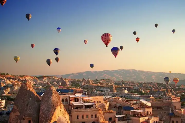 Dozens of hot air balloons spread across the morning sky above the cave-cut houses and rock cones of a Cappadocia town.