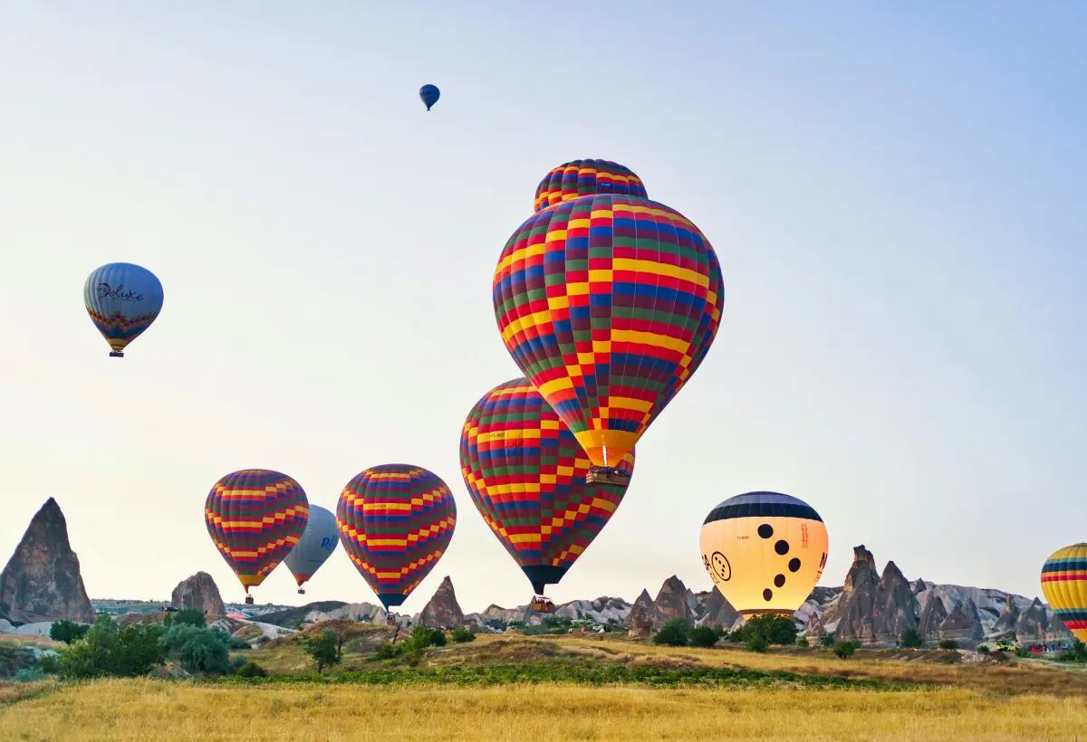 Boldly striped red and blue balloons hover just above a golden field in Cappadocia, a smiling face painted on the envelope of the balloon on the right.