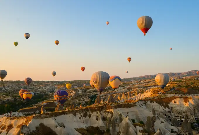 Hot air balloons drift over a Cappadocia valley of layered white and pink rock, the striped envelopes bright against the pale eroded slopes.