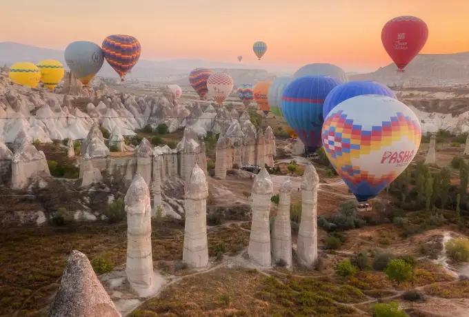 Balloons crowd the sunrise sky directly above the tall stone columns of Love Valley in Cappadocia, one passing only metres from the rock.