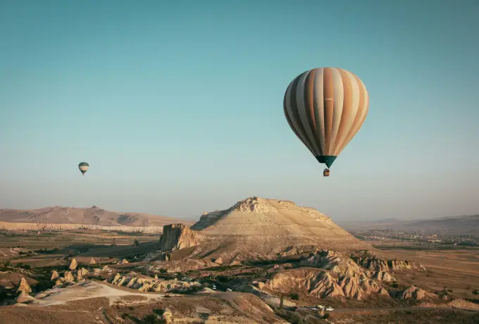 One hot air balloon floats alone above a flat-topped mesa in Cappadocia, the empty plateau stretching away under a soft teal sky.
