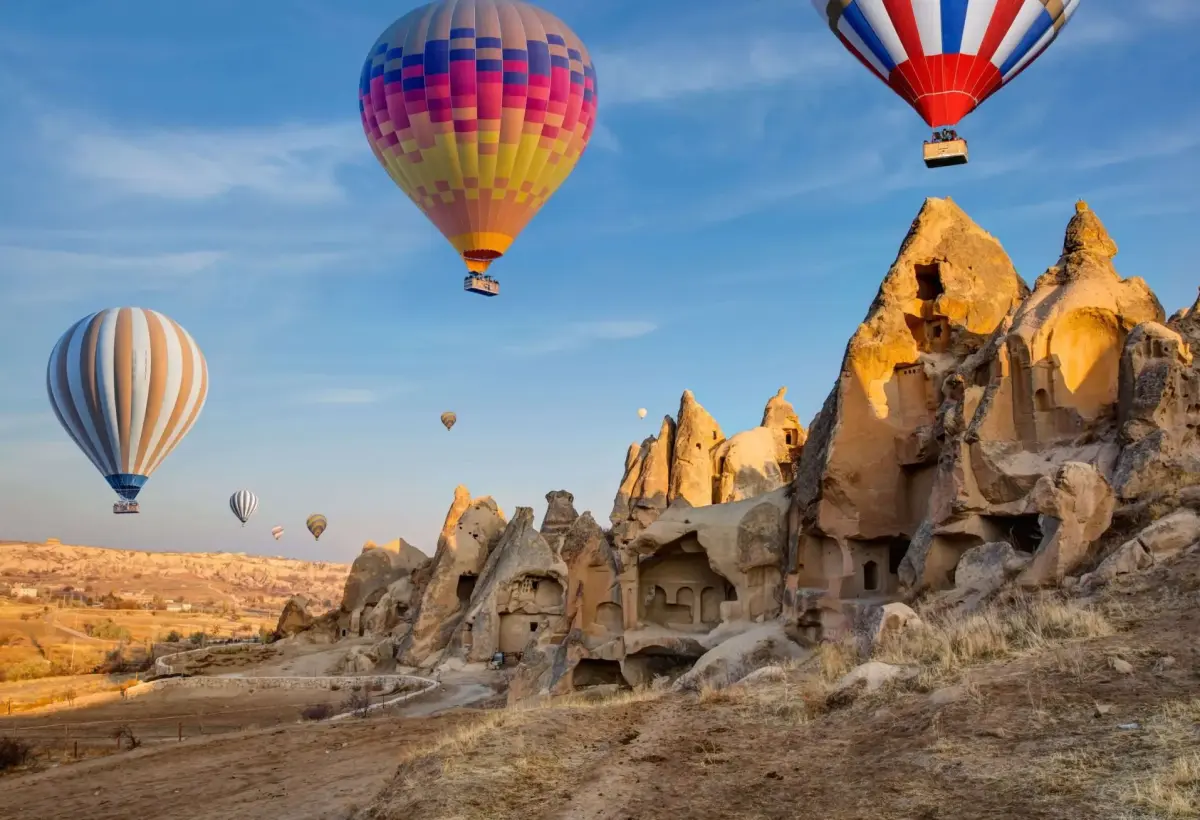 Two brightly striped balloons pass just above the jagged eroded rock formations of a Cappadocia valley on a clear morning.