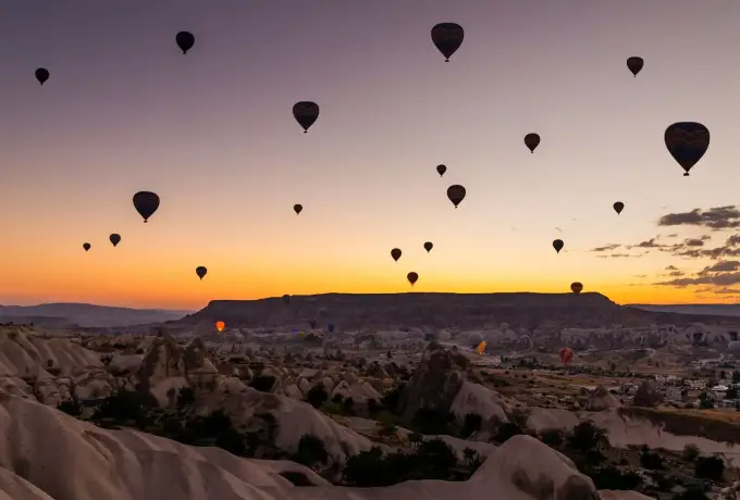 Hot air balloons read as black silhouettes against a band of sunrise gold above the still-dark valleys of Cappadocia.