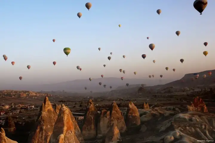 A wide fleet of hot air balloons floats above the multi-headed fairy chimneys of Monks Valley in Cappadocia in soft morning light.