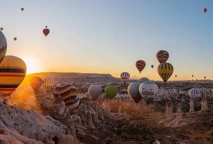 The first sunlight catches a group of hot air balloons still close to the ground in a Cappadocia valley of eroded rock and scrub.