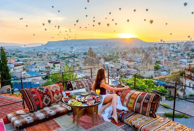 Kilim benches and a low breakfast table fill a Cappadocia terrace as the sun clears the ridge and balloons rise above the cave town.