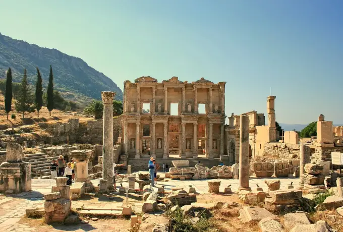 Scattered column drums and marble fragments fill the agora at Ephesus with the Library of Celsus standing beyond them.