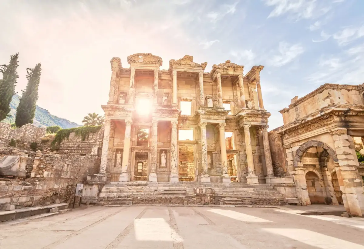 The sun breaks past the edge of the Library of Celsus at Ephesus, throwing a bright star of light across the empty forecourt.