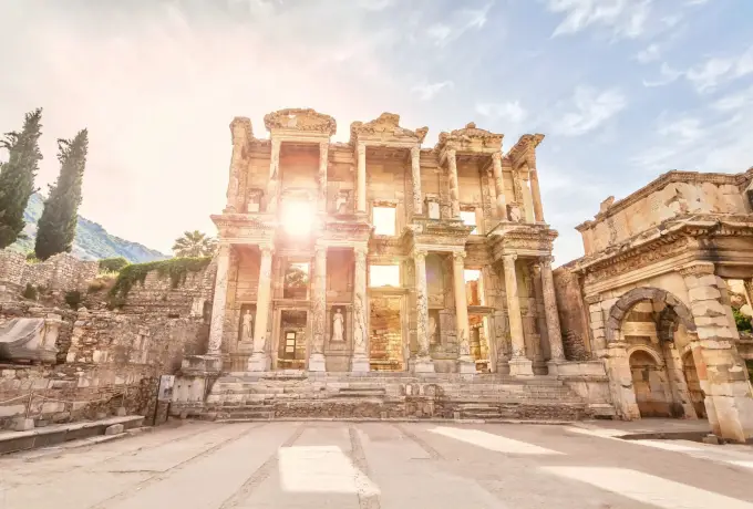The sun breaks past the edge of the Library of Celsus at Ephesus, throwing a bright star of light across the empty forecourt.