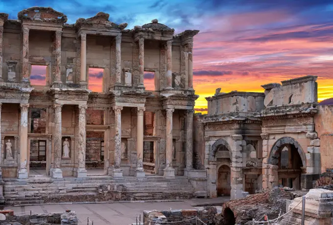A fiery orange sunset burns behind the Library of Celsus at Ephesus, turning its stonework deep burnished gold.