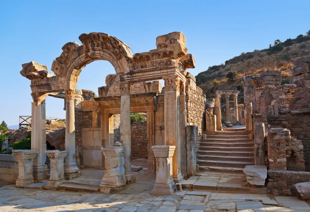 The ornate carved arch of the Temple of Hadrian stands on Curetes Street at Ephesus with steps climbing behind it.
