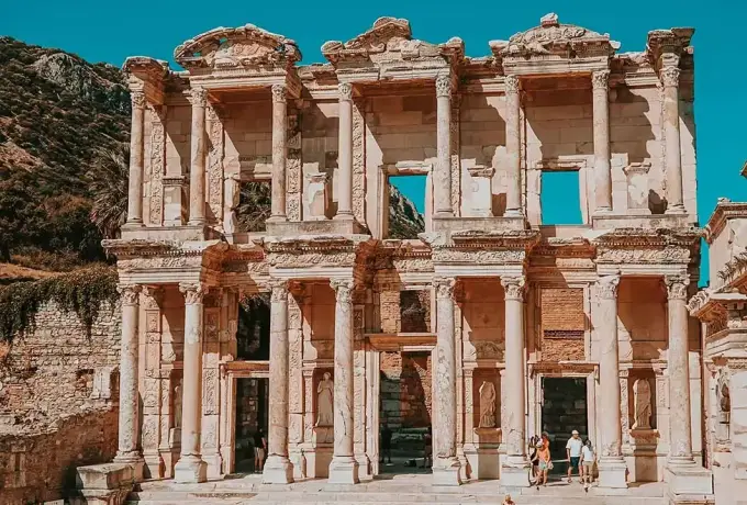 A close frontal view of the Library of Celsus at Ephesus under a vivid turquoise sky, the rocky hillside just above the roofline.
