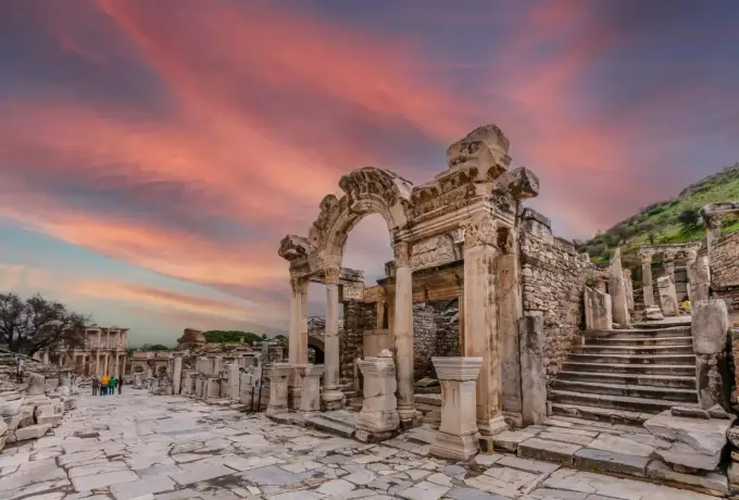 Pink and violet cloud streaks the sky above the carved arch of the Temple of Hadrian on Curetes Street at Ephesus.