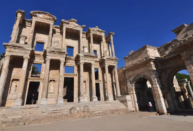 A low wide-angle view sets the Library of Celsus and the Roman gate at Ephesus against a deep clear blue sky above an empty forecourt.