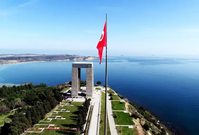 An aerial view shows the Canakkale Martyrs Memorial and its flagpole standing on the headland above the calm strait.