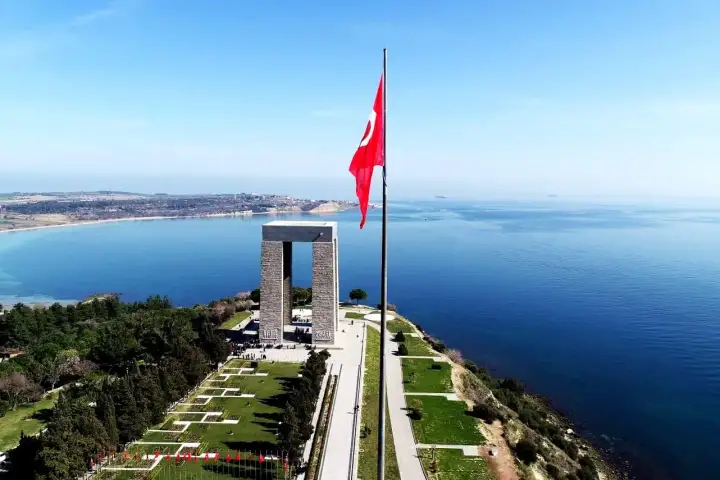 An aerial view shows the Canakkale Martyrs Memorial and its flagpole standing on the headland above the calm strait.