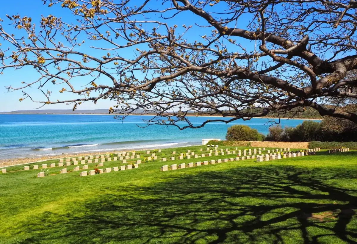 A cemetery of pale headstones lies on the green slope directly above the turquoise water of the Gallipoli coast.