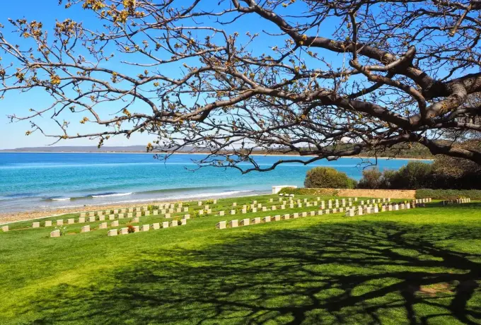 A cemetery of pale headstones lies on the green slope directly above the turquoise water of the Gallipoli coast.