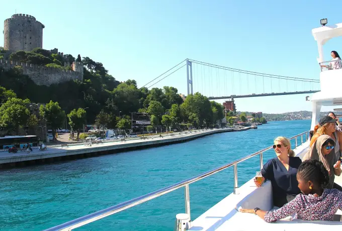 A cruise boat runs up the Bosphorus in Istanbul past the towers of the old fortress with the second bridge ahead.
