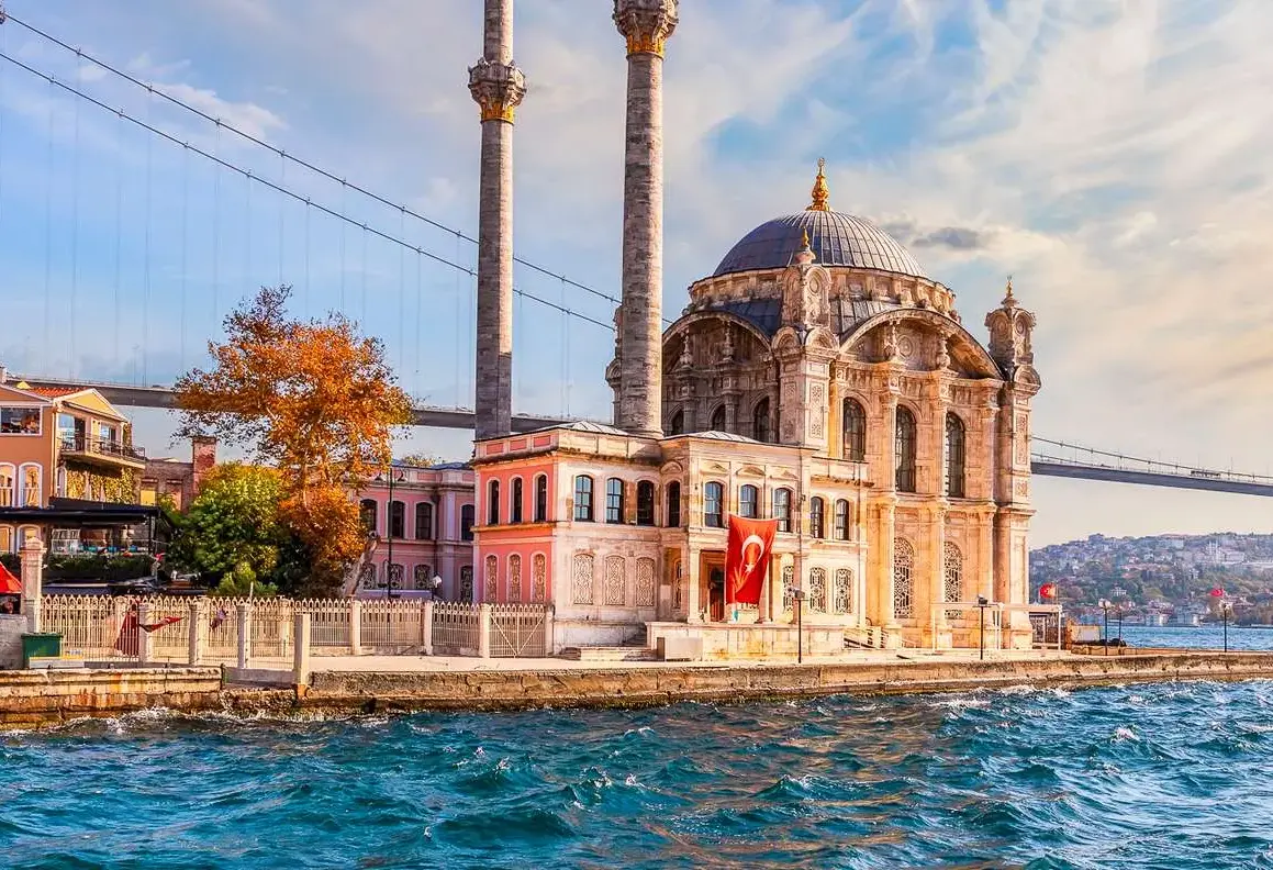 Ortakoy Mosque stands at the water's edge in Istanbul with the suspension bridge rising directly behind it.