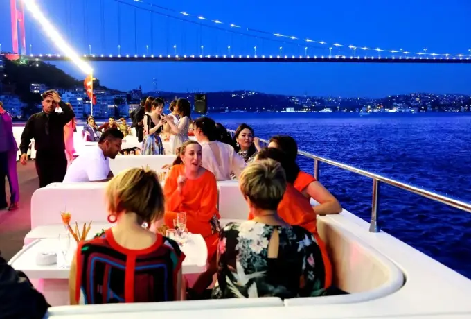 Guests dine on the open deck of a Bosphorus cruise in Istanbul as the illuminated bridge stretches across the night sky.