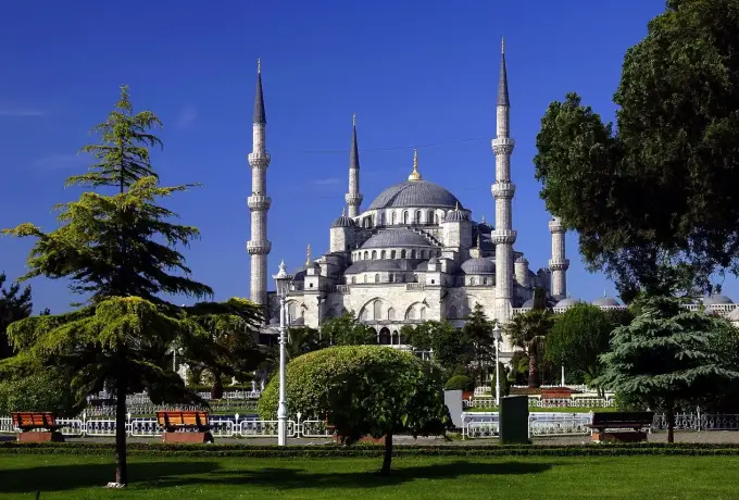 The Blue Mosque rises above the mown lawns and mature trees of the Sultanahmet gardens in Istanbul under a deep blue sky.