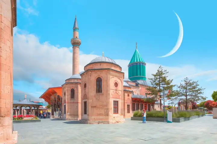 A crescent moon hangs in the bright sky above the octagonal mosque, minaret and turquoise dome of the Mevlana complex in Konya.