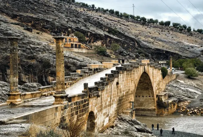The single Roman arch of the Cendere bridge spans a rocky river gorge near Nemrut with two columns standing at its end.