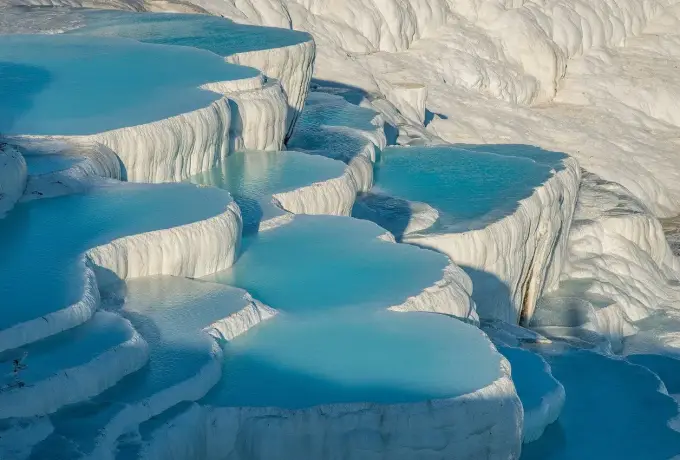 Rounded white travertine basins filled with turquoise thermal water stack down the hillside at Pamukkale, filling the whole frame.