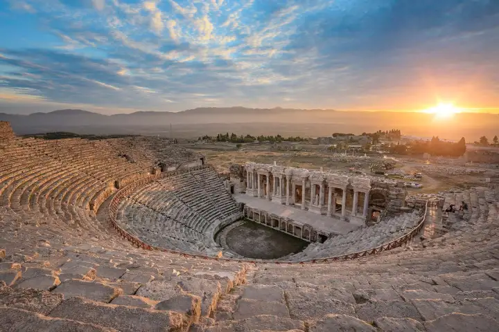 The sun rises behind the Hierapolis theatre at Pamukkale, lighting its seating tiers and the plain beyond.