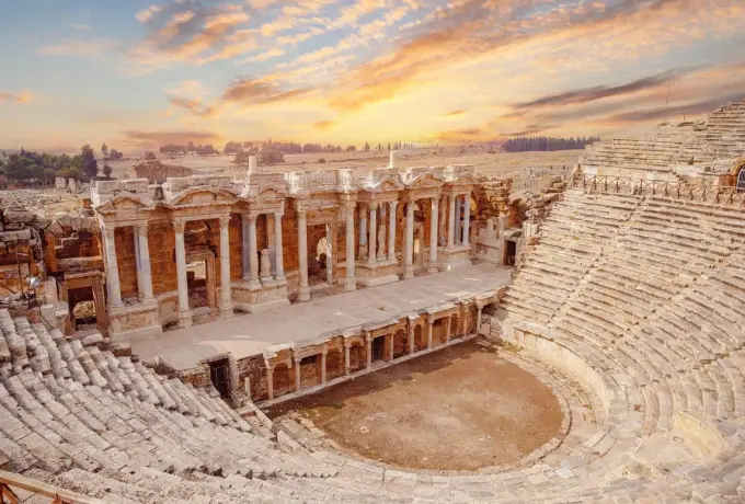 Warm light picks out the columns and niches of the stage facade at the Hierapolis theatre above its curved seating.