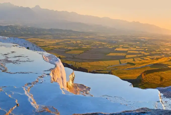 The white terrace rim at Pamukkale catches the light above the wide golden farmland of the plain below.