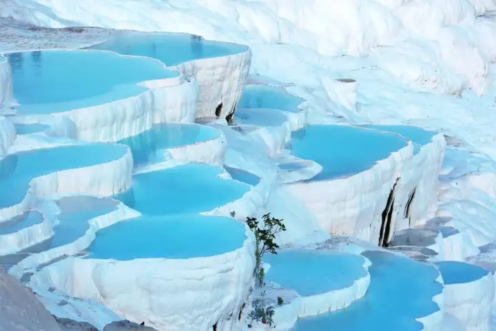 Rounded white basins hold vivid blue mineral water in stacked layers across the Pamukkale hillside.