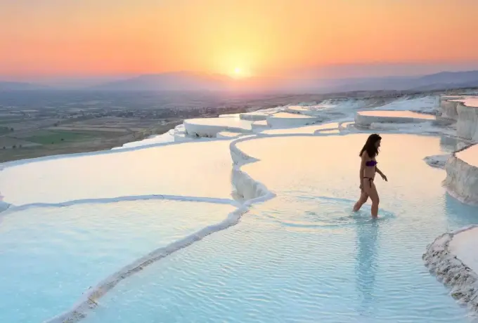 Layered white travertine terraces and turquoise pools cascade down the Pamukkale hillside under a vivid blue sky.