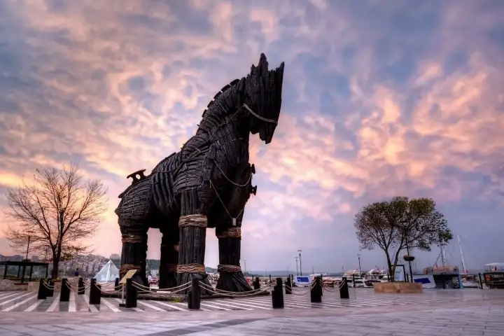 The dark timber Trojan horse on the Canakkale waterfront stands against a pink and violet sunset over the strait.